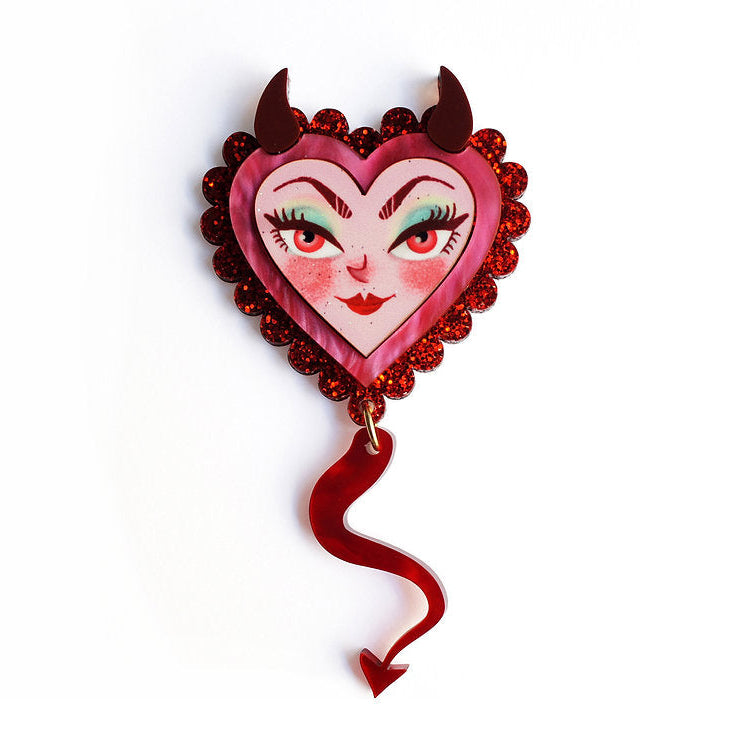 Heart-shaped brooch with devil face design on a white background