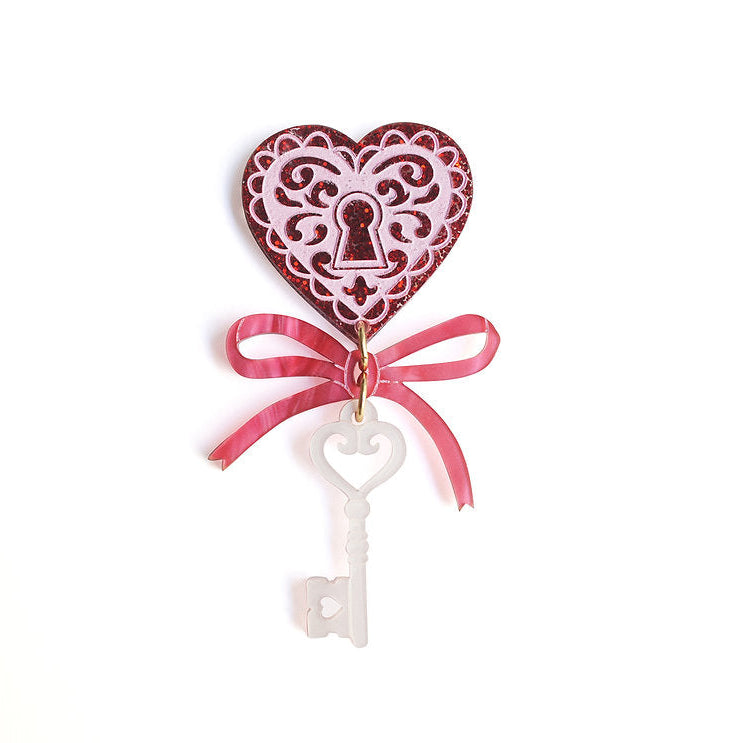 Decorative heart-shaped keychain with a white key and pink ribbon on a white background