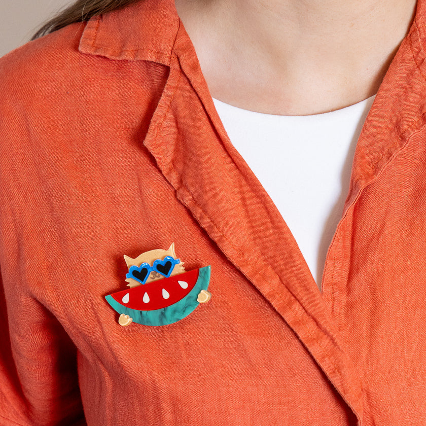 Person wearing an orange shirt with a watermelon-themed brooch.
