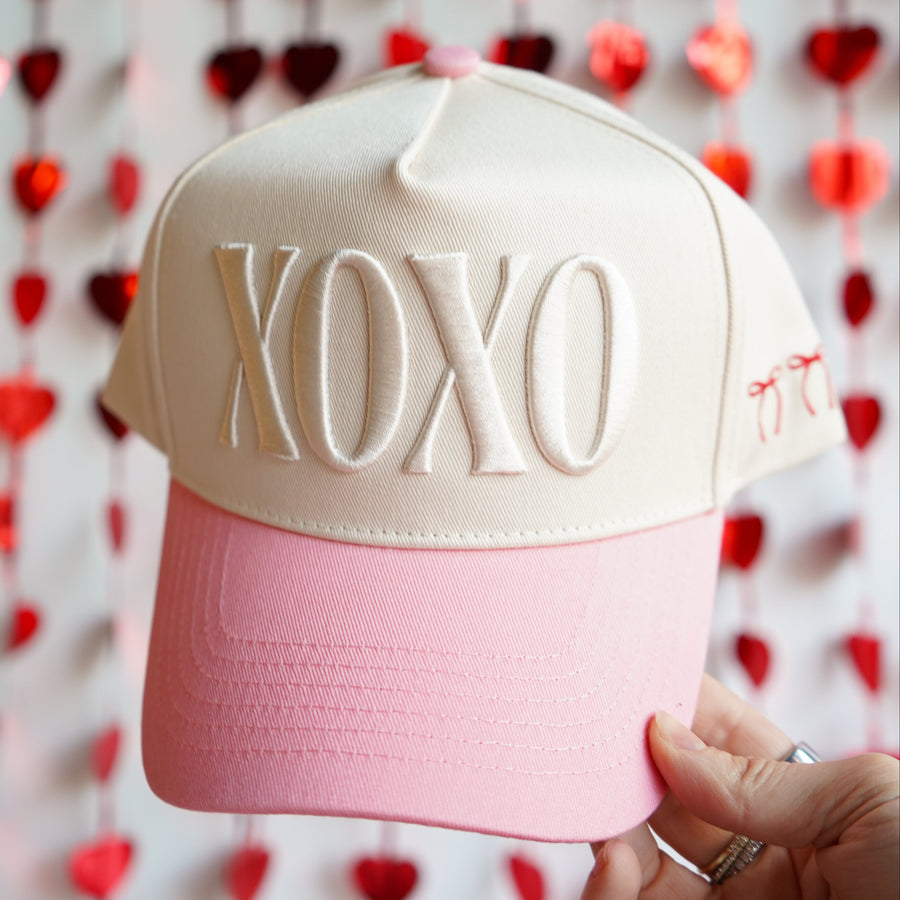 Beige and pink cap with 'XOXO' text held against a heart-patterned background