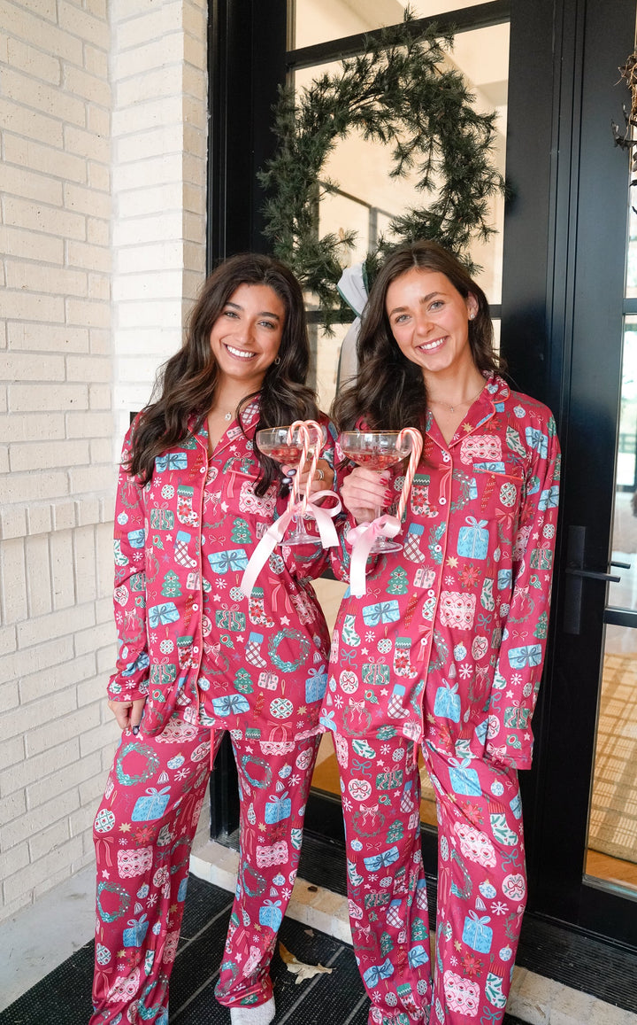 Two women wearing pink pajamas with a festive pattern, standing in front of a door with a wreath.