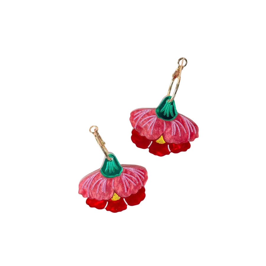 A pair of handmade flower-shaped earrings with pink and red petals, green centers, and gold-tone hooks, displayed on a light pink background with decorative felt leaves.