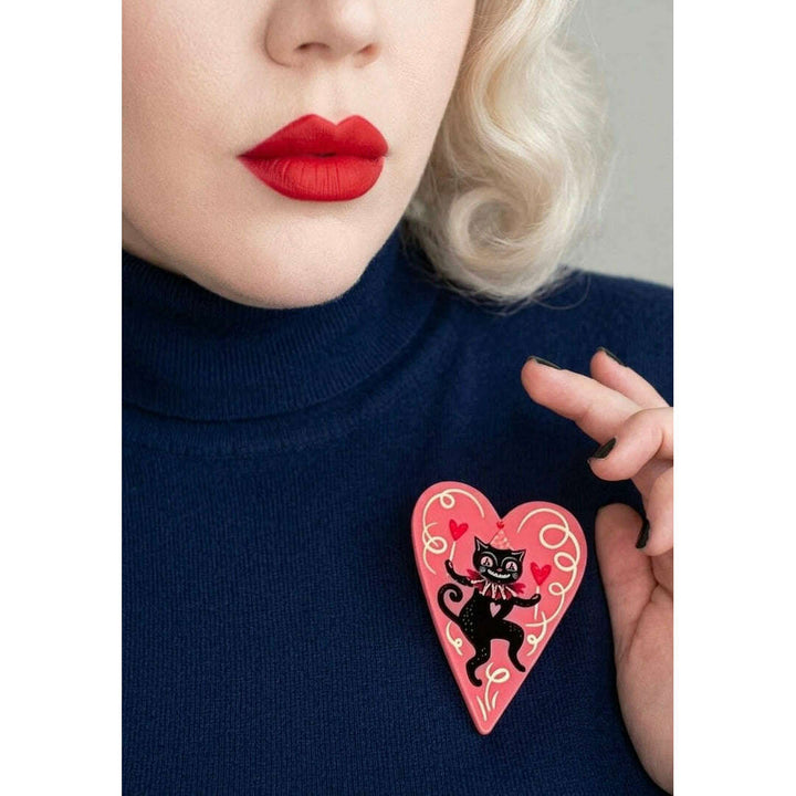 Person wearing a black turtleneck with a pink heart-shaped brooch featuring a black cat design by Johanna parker