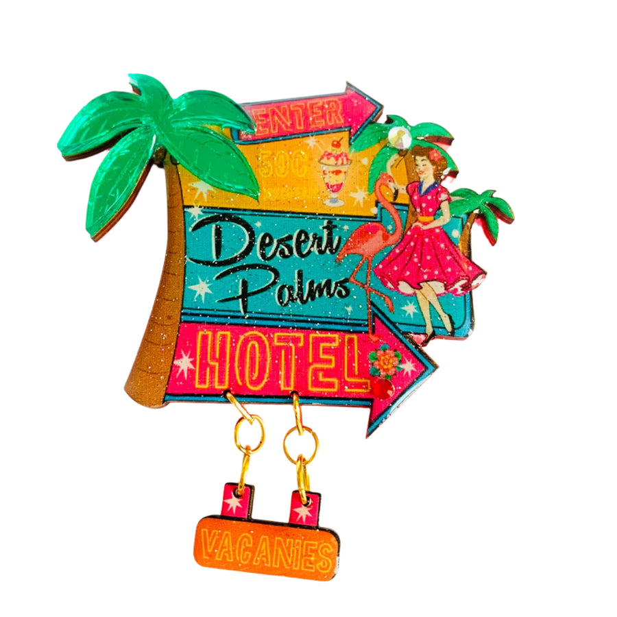 Colorful brooch with 'Desert Palms Hotel' design, palm trees, and a suitcase.