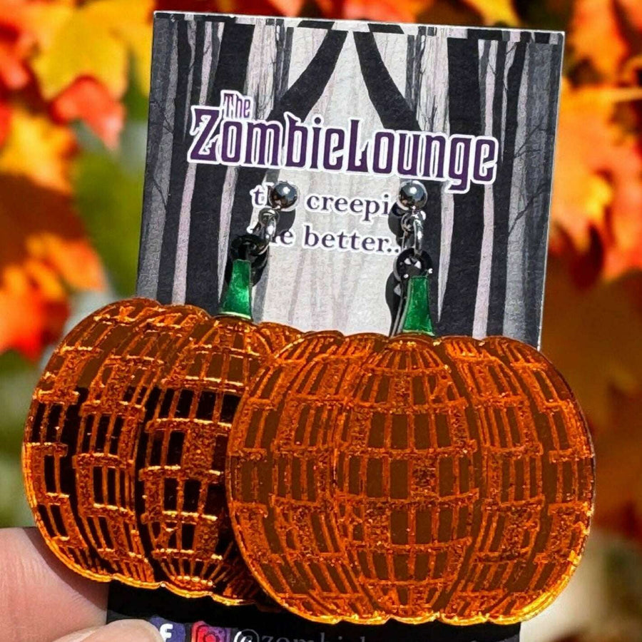 Pumpkin-shaped earrings on a card held in front of autumn leaves
