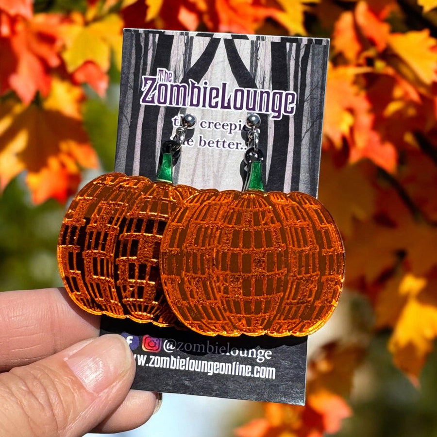 Pumpkin-shaped earrings on a card held in front of autumn leaves