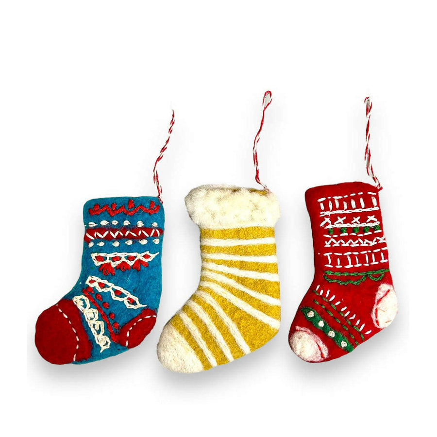 A set of three felted wool Christmas stocking ornaments with embroidered designs, including a red and white stocking with a white cuff, a blue and yellow stocking with a yellow cuff, and a green and red stocking with a red cuff. Each ornament has a hanging ribbon and is against a white background.