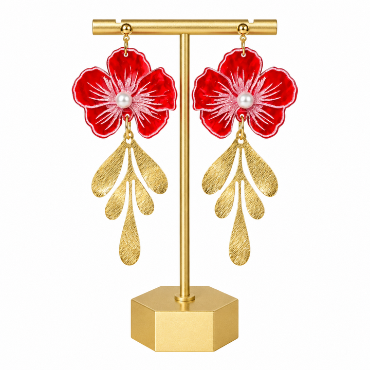 A pair of dangling earrings displayed on a gold stand against a white background. Each earring features a glossy red flower with white petal details, a small white pearl at the center, and three textured gold leaf-like drops below.