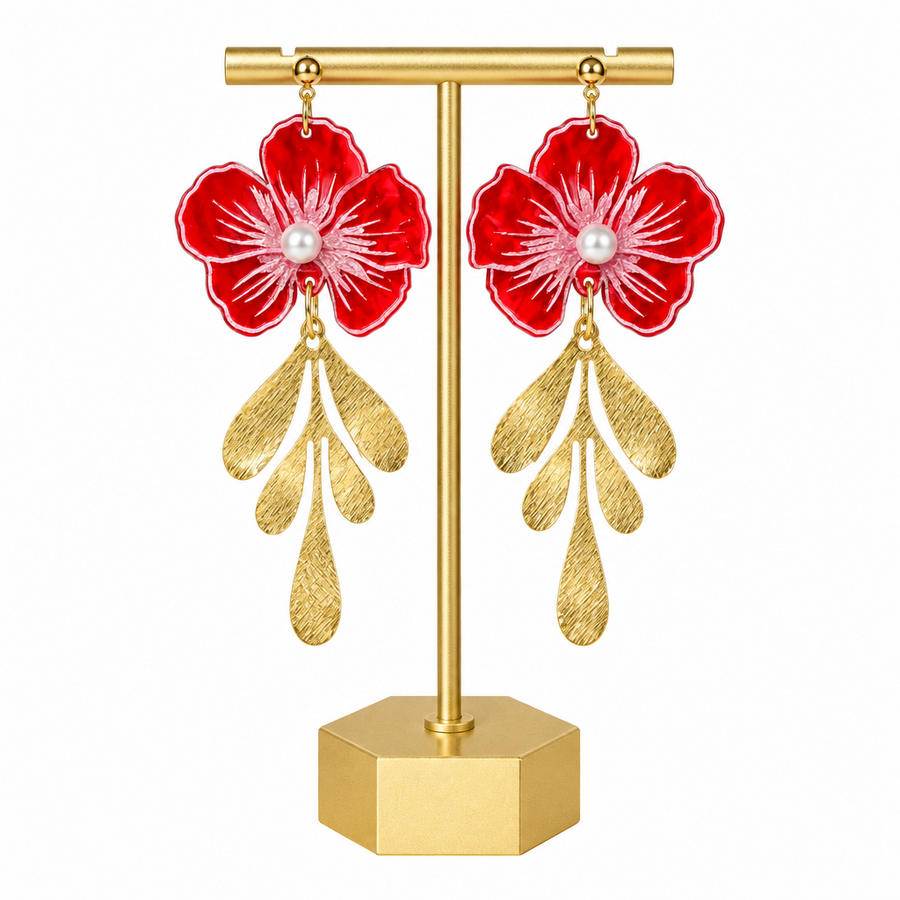 A pair of dangling earrings displayed on a gold stand against a white background. Each earring features a glossy red flower with white petal details, a small white pearl at the center, and three textured gold leaf-like drops below.