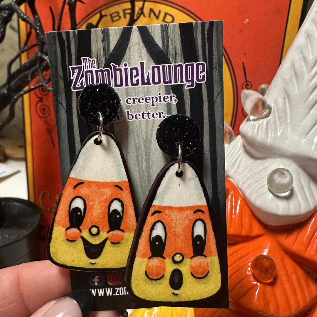Pair of candy corn-shaped earrings with a 'Zombie Lounge' label against a Halloween-themed background.