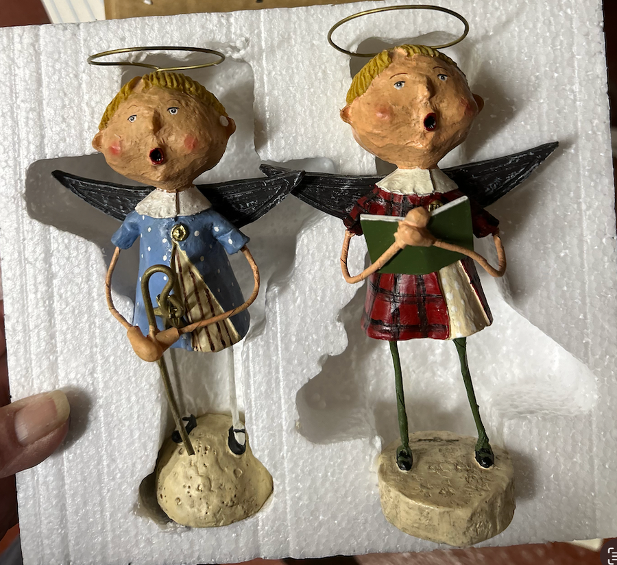 Two angel figurines on a white surface, one playing a trumpet and the other holding a book.