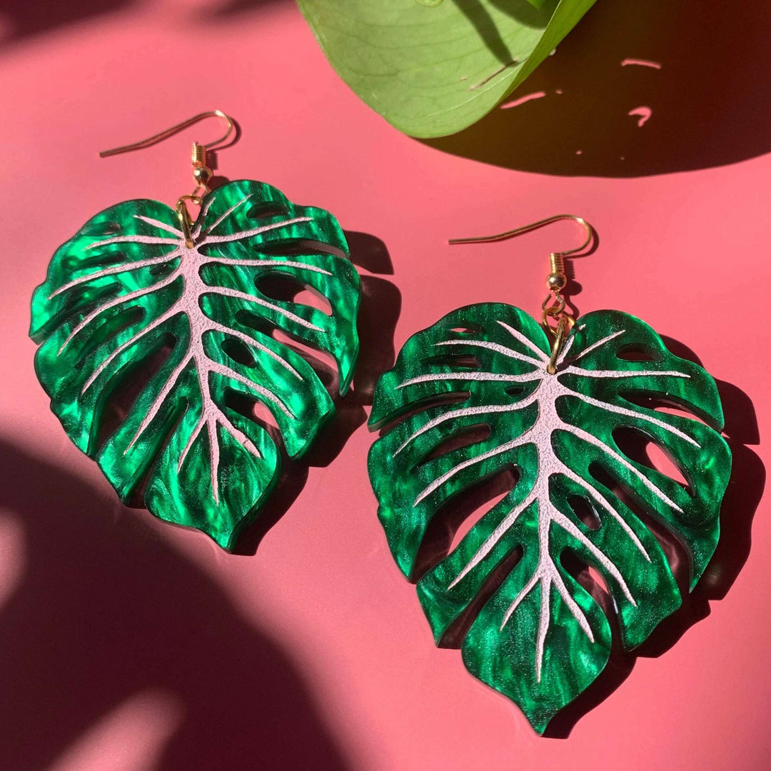 Green leaf-shaped earrings on a pink surface with a green leaf