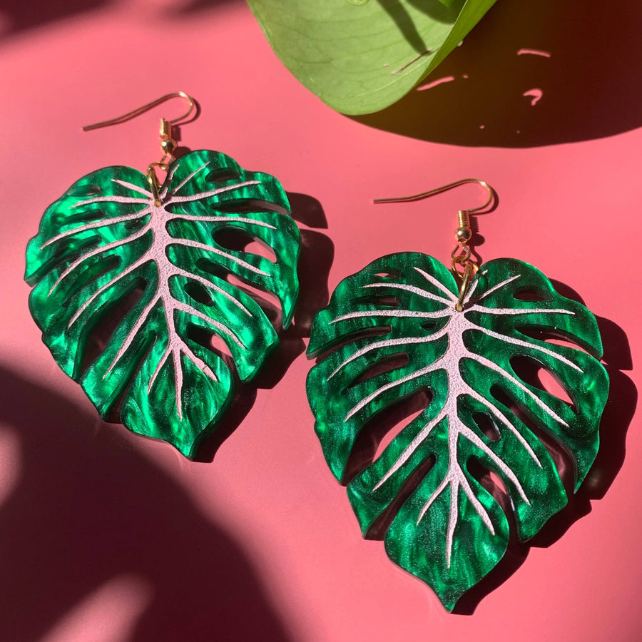 Green leaf-shaped earrings on a pink surface with a green leaf