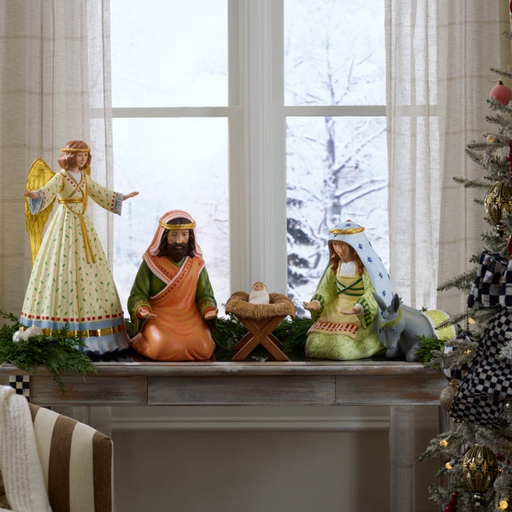 Nativity scene on a fireplace mantle with a decorated Christmas tree in the background.