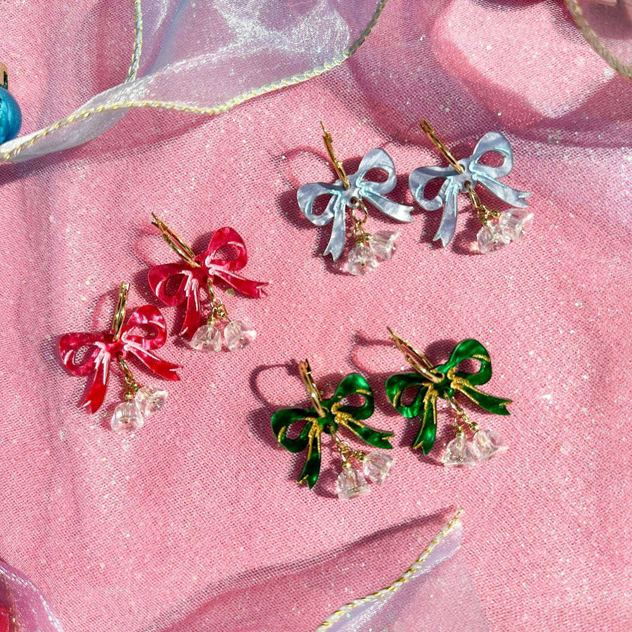 Colorful bow-shaped earrings on a pink fabric background