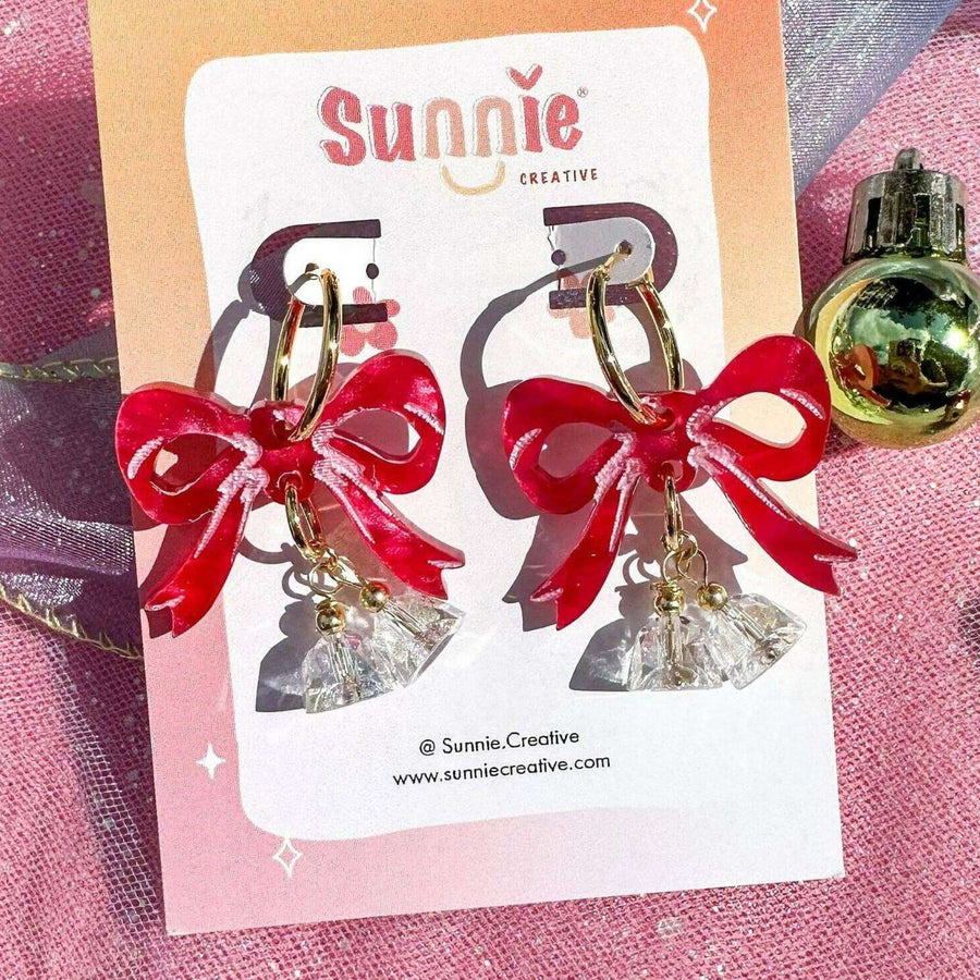 Earrings with red bows and gold and blue accents on a pink glittery background