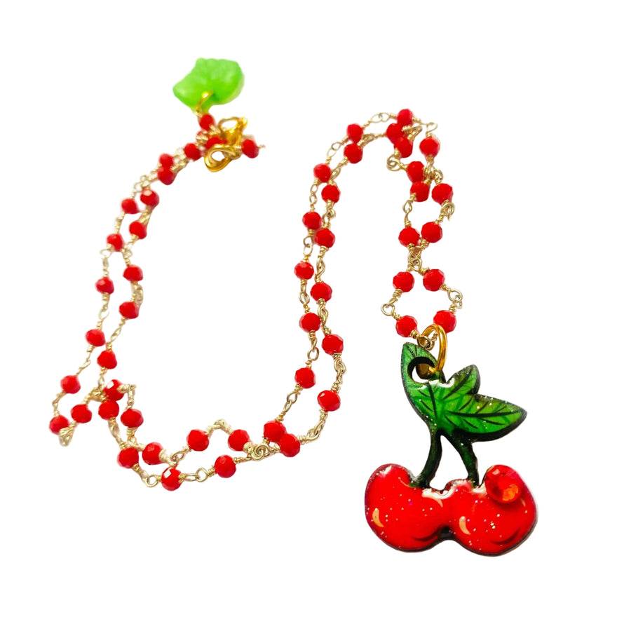 A beaded necklace with red beads and a cherry-shaped pendant, displayed on a light gray background.