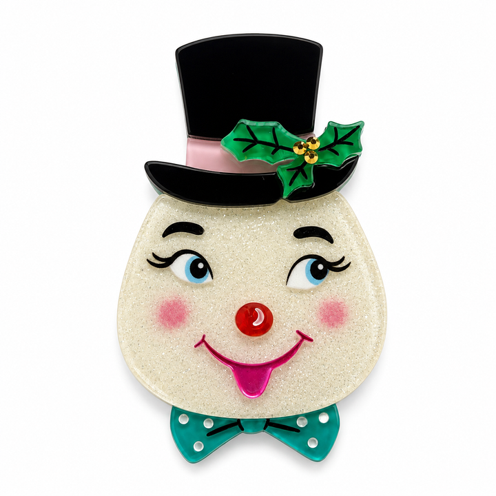 A festive snowman face brooch with a glittery cream body, black top hat, green holly leaves, blue eyes, pink cheeks and tongue, and a teal polka-dot bow tie on a white background.